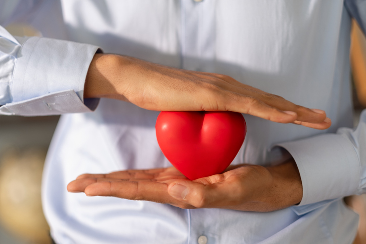 Businessman is protecting a red heart with his hands, symbolizing insurance, healthcare and wellbeing