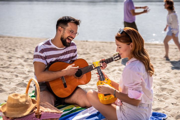 Friends play ukulele and guitar on a picnic on a beach.
