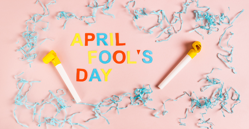 April Fools' Day from colored letters, whistles, balloons and paper on pink top view web banner