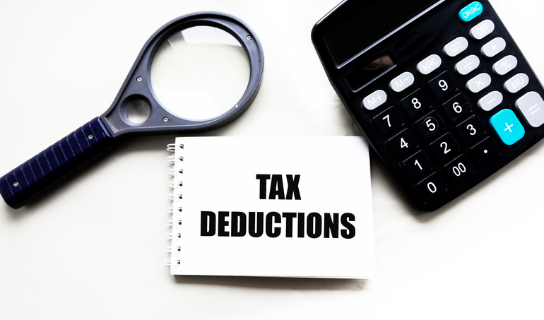 TAX DEDUCTIONS are words in a notebook on the background of a calculator and a magnifying glass .business concept