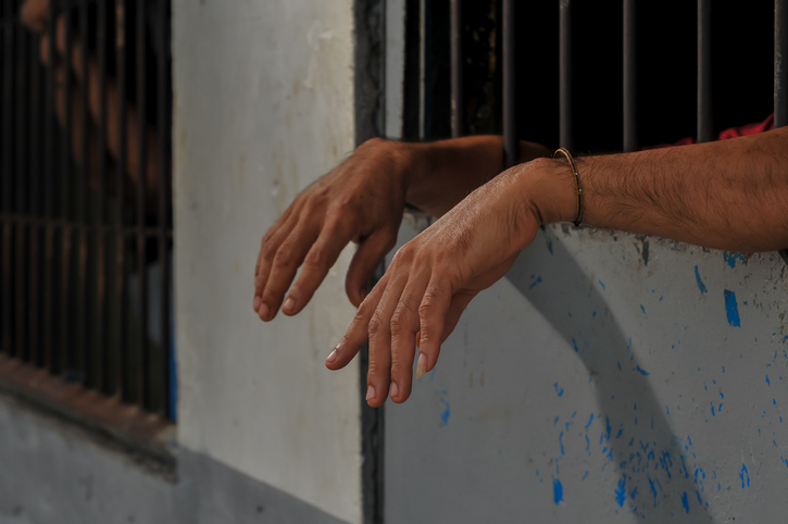 hands of a prisoner behind prison bars on black background