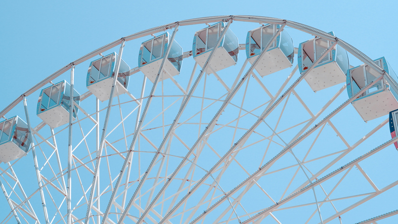 Close view of Ferris wheel cabins on sunny sky background in park setting.