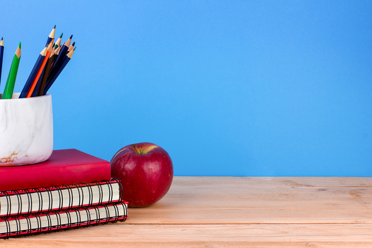 Notebooks, pencils, apple on wooden desk. Education and learning concept on blue background