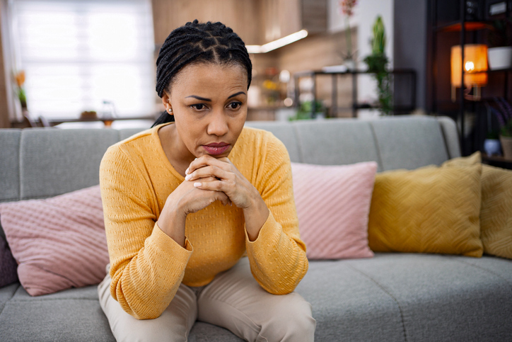 Sad woman sitting on the sofa at home is feeling lonely and depressed