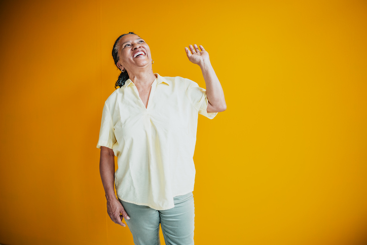 Senior woman laughing joyfully indoors against a vibrant yellow background with a bright smile