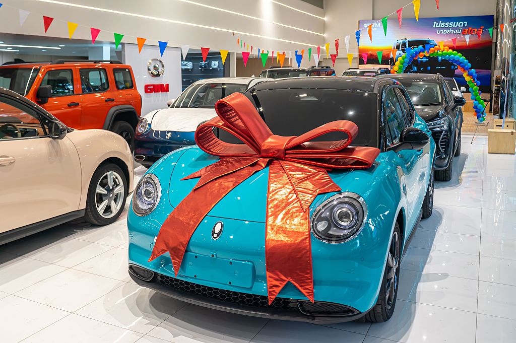 A turquoise GWM Ora car with a large red bow sits among other vehicles in a showroom, Bangkok, Thailand