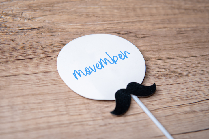 A white oval paper with the word Movember attached to a stick and mustache cutout.