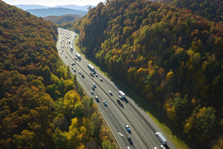 Aerial view of I-40 freeway in North Carolina heading to Asheville through Appalachian mountains in golden fall with moving trucks and cars. Interstate transportation concept