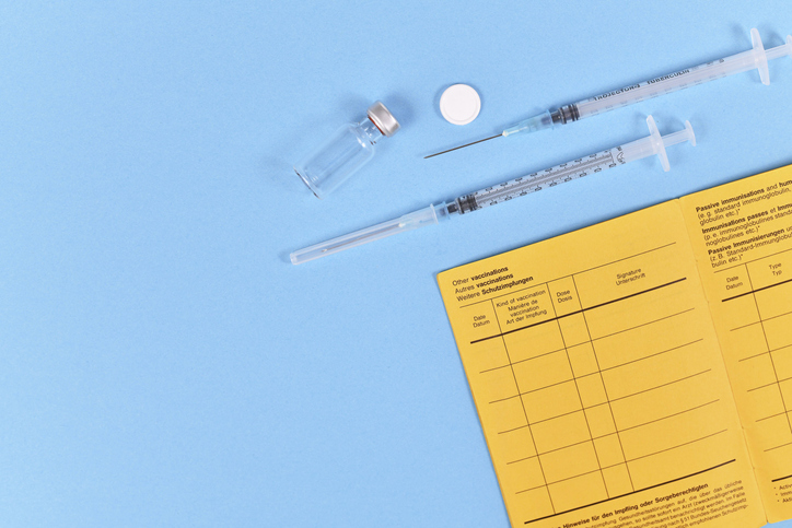 Vaccine concept with syringe, vial and yellow international certificate of vaccination on blue background with copy space