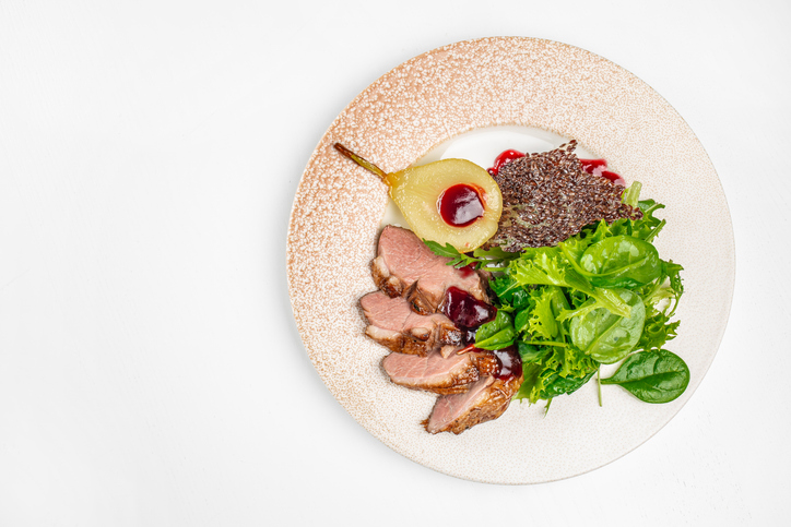 Elegant gourmet dish of roasted duck breast served with caramelized pear, fresh green salad mix, berry sauce and crispy garnish. festive menus, or gourmet food concepts