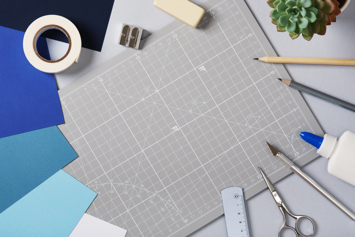 Gray cutting mat surrounded by colored paper and craft tools on a desk. Creative workspace for art and handmade design preparation.