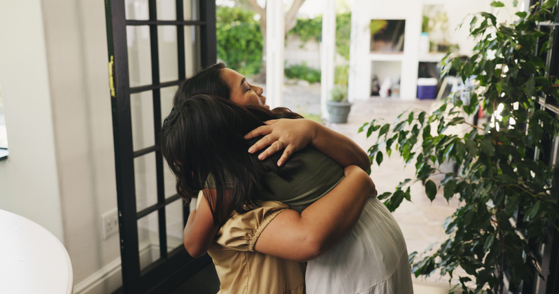 Mother, child or hug with greeting in home for love, safety or care together by door or entrance. Mom, kid or daughter with smile, parent or guardian for embrace, farewell or holiday goodbye in house