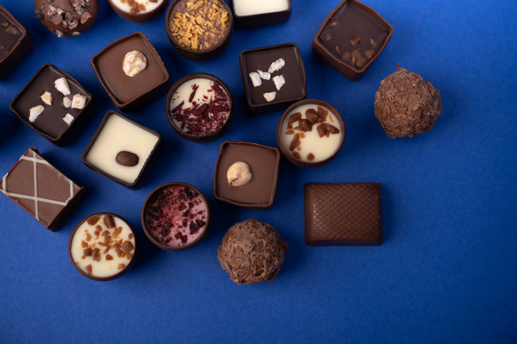 assorted gourmet chocolate pralines and truffles artistically arranged in a studio flatlay on a vivid cobalt-blue background, highlighting glossy ganache, textured shells, nuts, sprinkles and creamy f