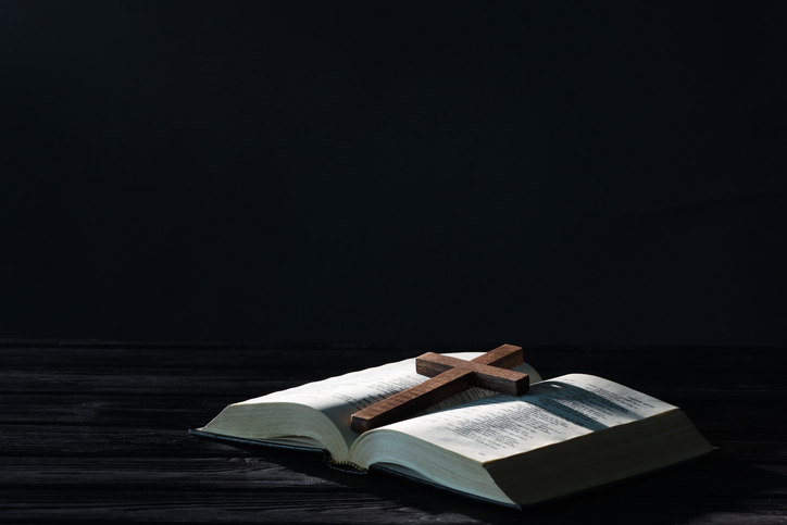 Bible and cross on black wooden table against dark background, space for text. Religion of Christianity