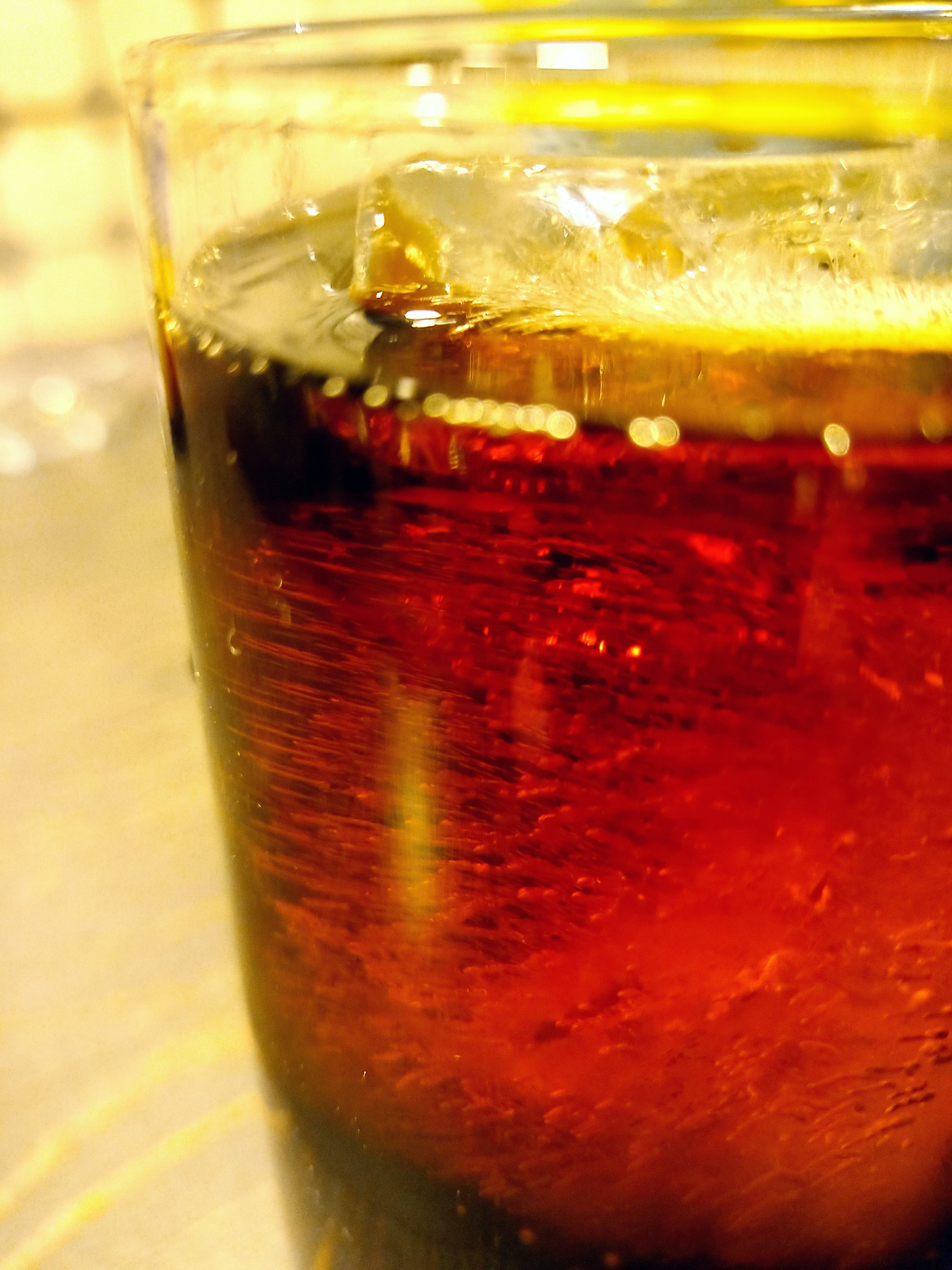 a glass of whiskey with Coke and ice on the table with drops