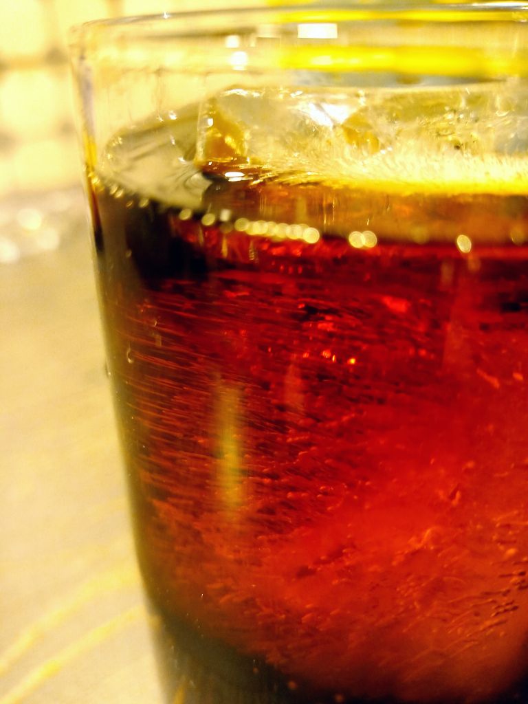 a glass of whiskey with Coke and ice on the table with drops