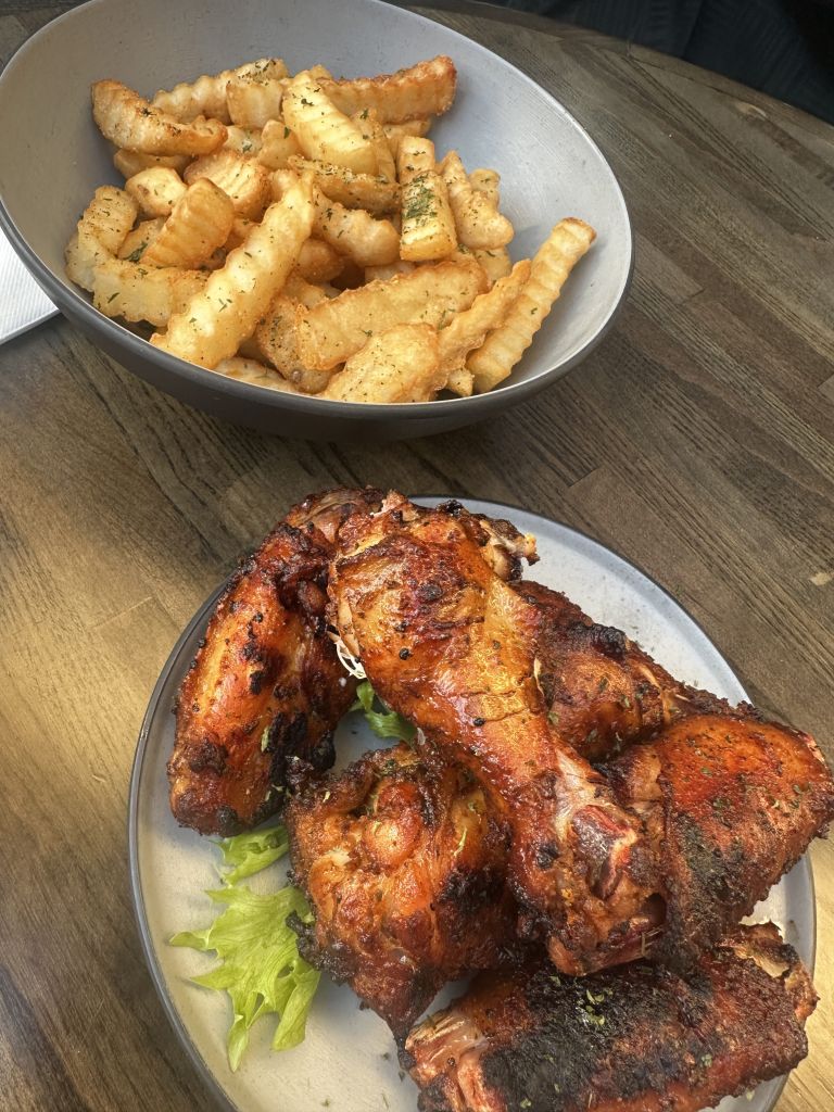 A plate of golden, crispy french fries and a plate of roasted, saucy chicken on a wooden table.