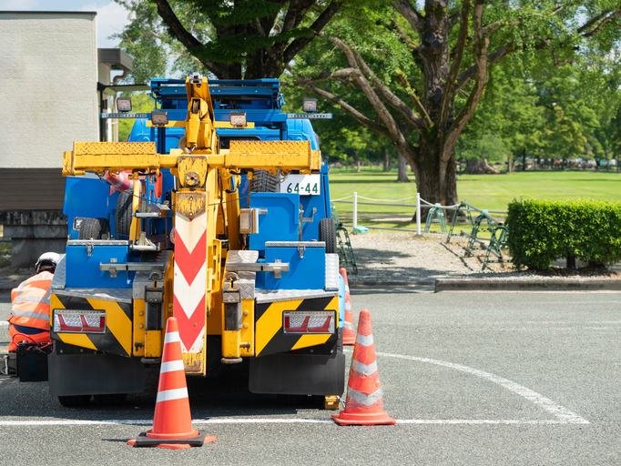Tow truck or breakdown service vehicle with safety orange cones parked outdoor near a park.