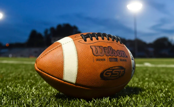 A football on a grassy field at night, with the Wilson brand name visible.