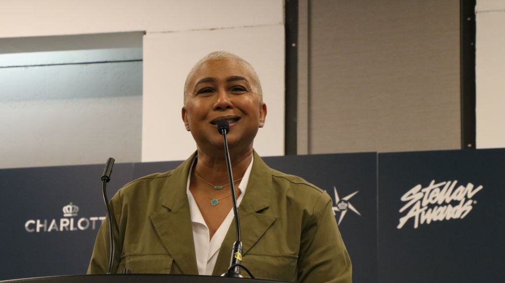 A smiling person speaking into a microphone on a stage with "Charlotte" and "Stellar Awards" branding visible.