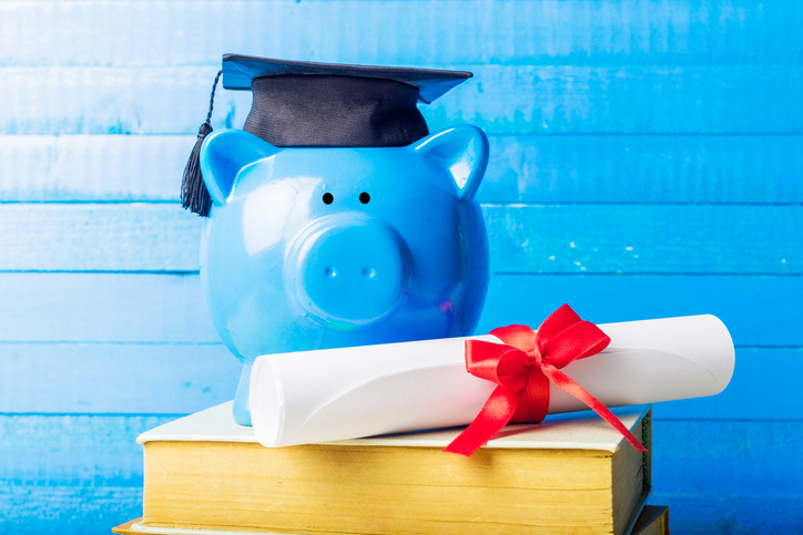 Bright blue piggy bank with graduation cap and diploma on stack of books