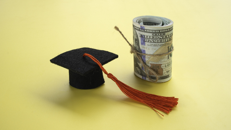 Graduation Mortarboard Cap Beside Rolled Dollar Bills Tied with String Concept of College Tuition Savings and Student Loan